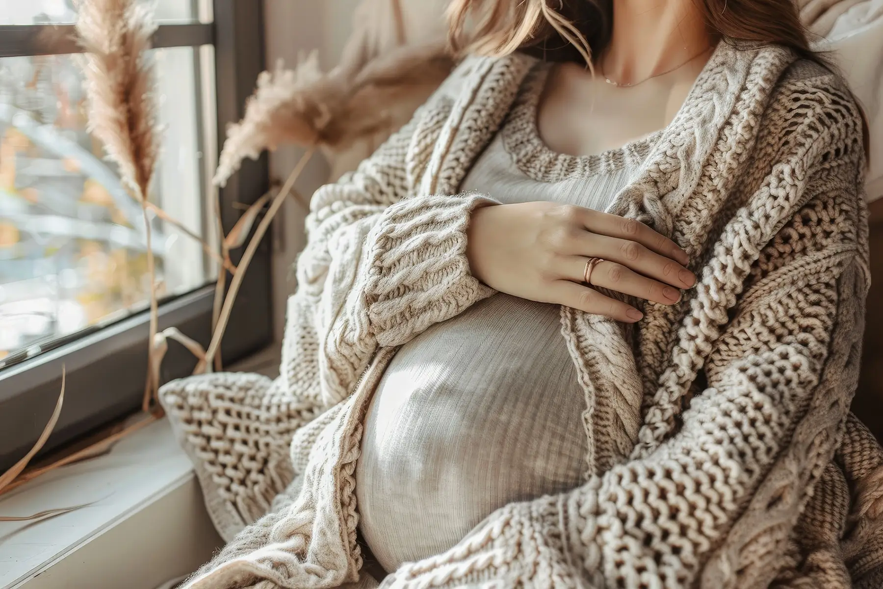 Schwangere Frau mit Strickjacke hält liebevoll ihren Babybauch und Hebamme Kai Esther Schlender im Wald mit natürlicher Atmosphäre und freundlichem Blick